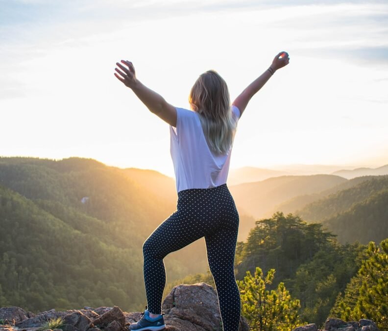 woman in white shirt and black pants standing on rocky mountain during daytime